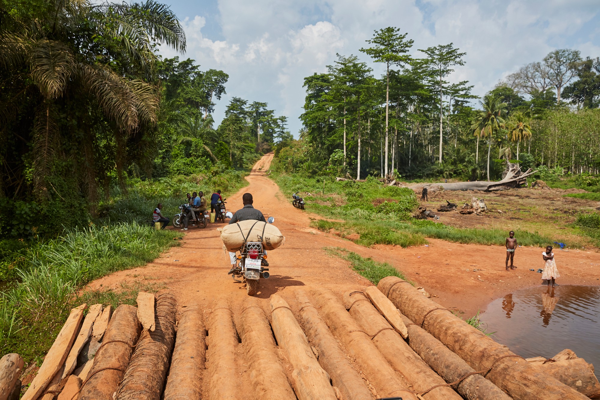 Man on a scooter that has a brown burlap bag attached to it on a rural road